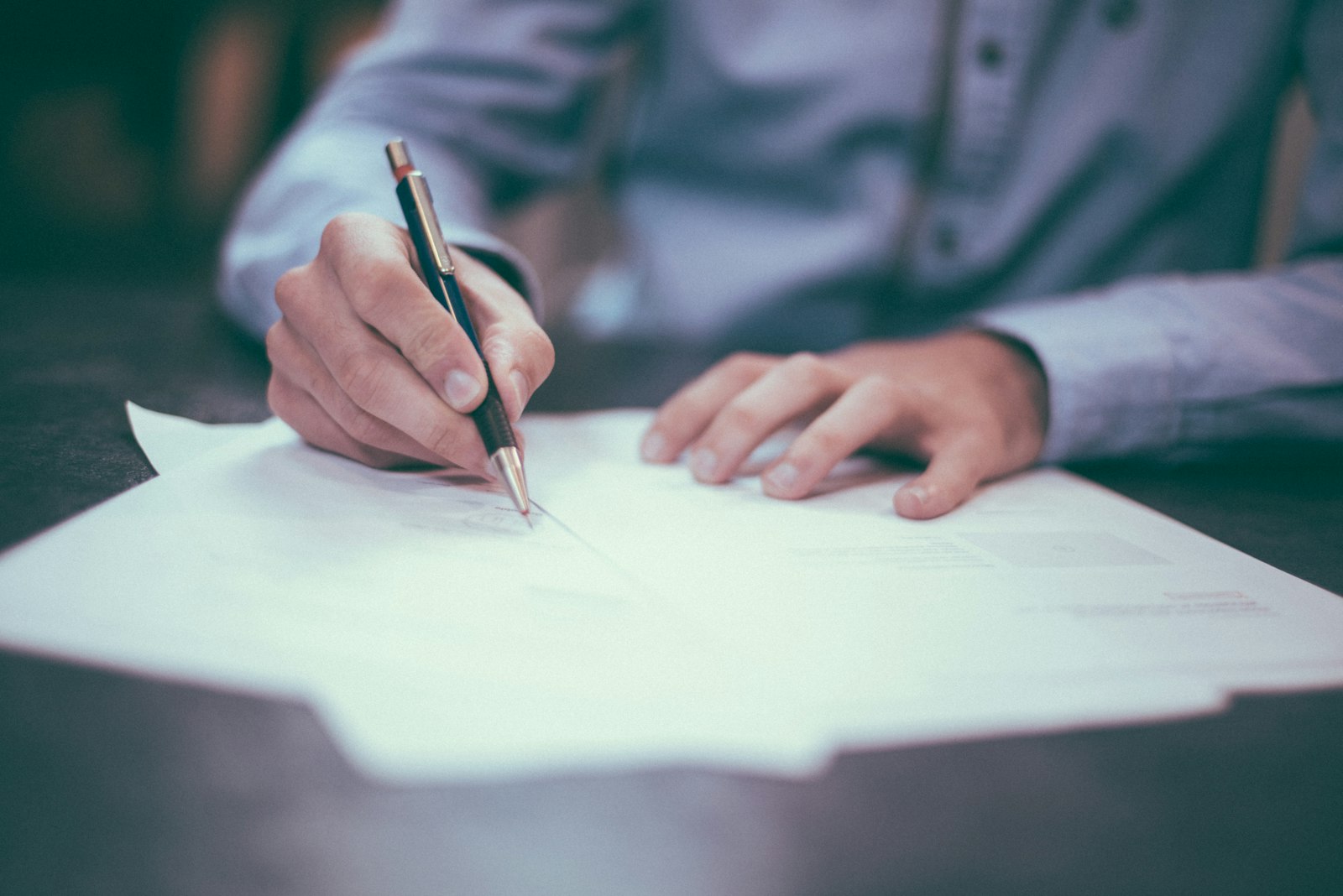 A person signing a paper document with a pen at a desk, representing an open letter