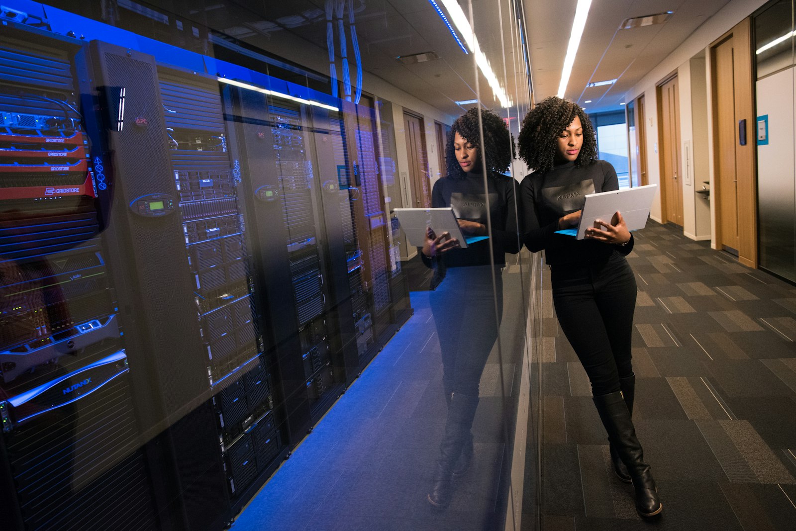 A woman holding a tablet walks along a corridor lined with illuminated server racks in a data centre