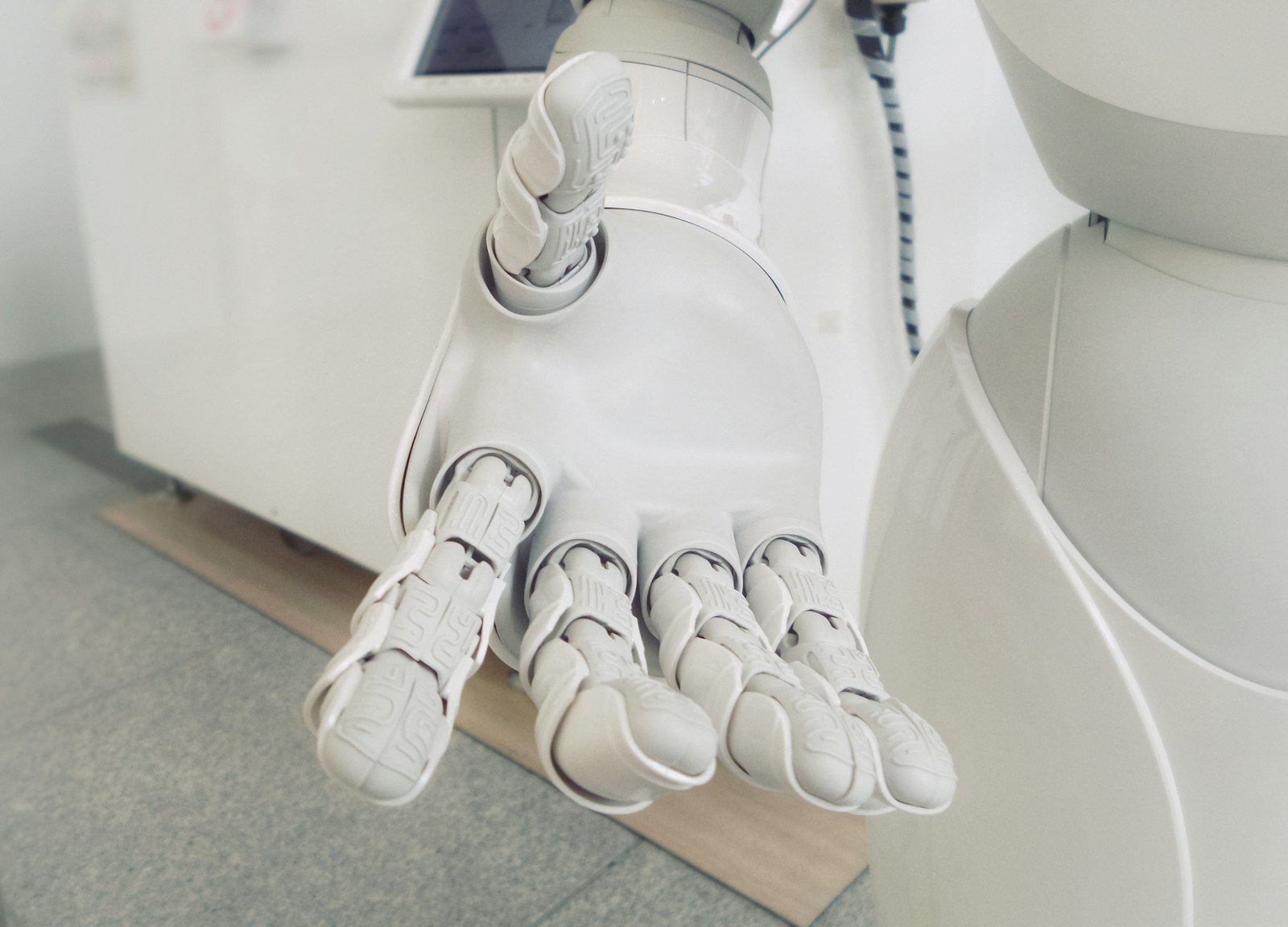 A white humanoid robot hand held open palm up in a bright room
