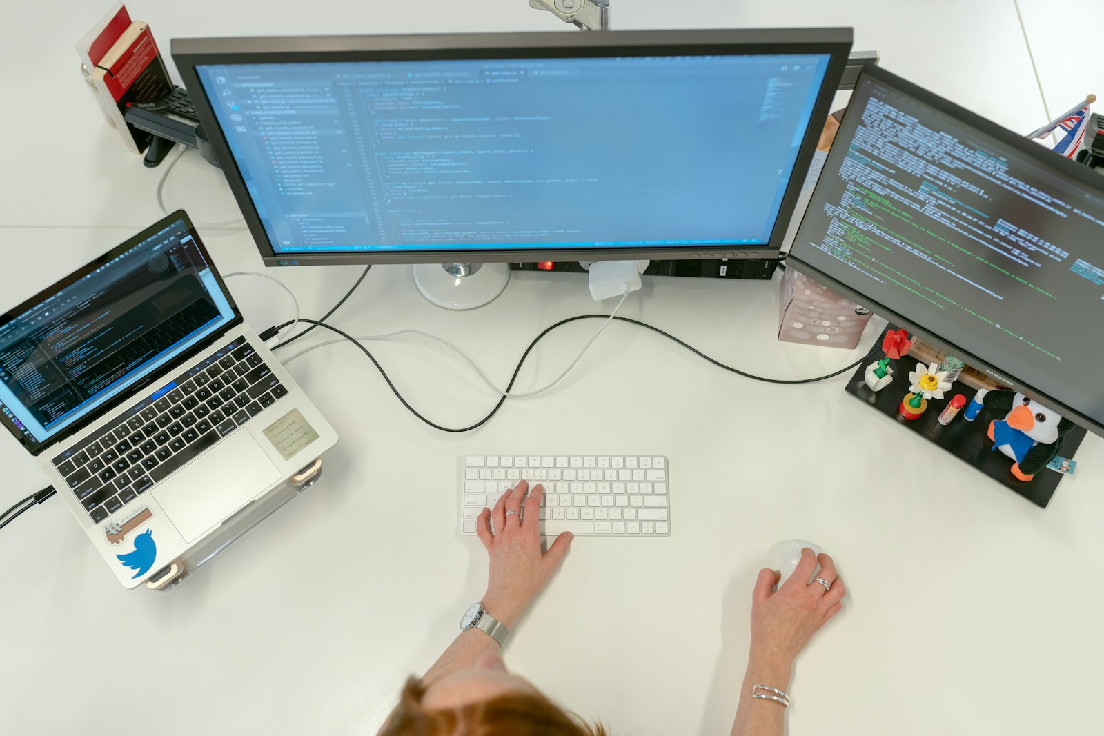 Overhead view of a developer workstation with two monitors and a laptop showing code