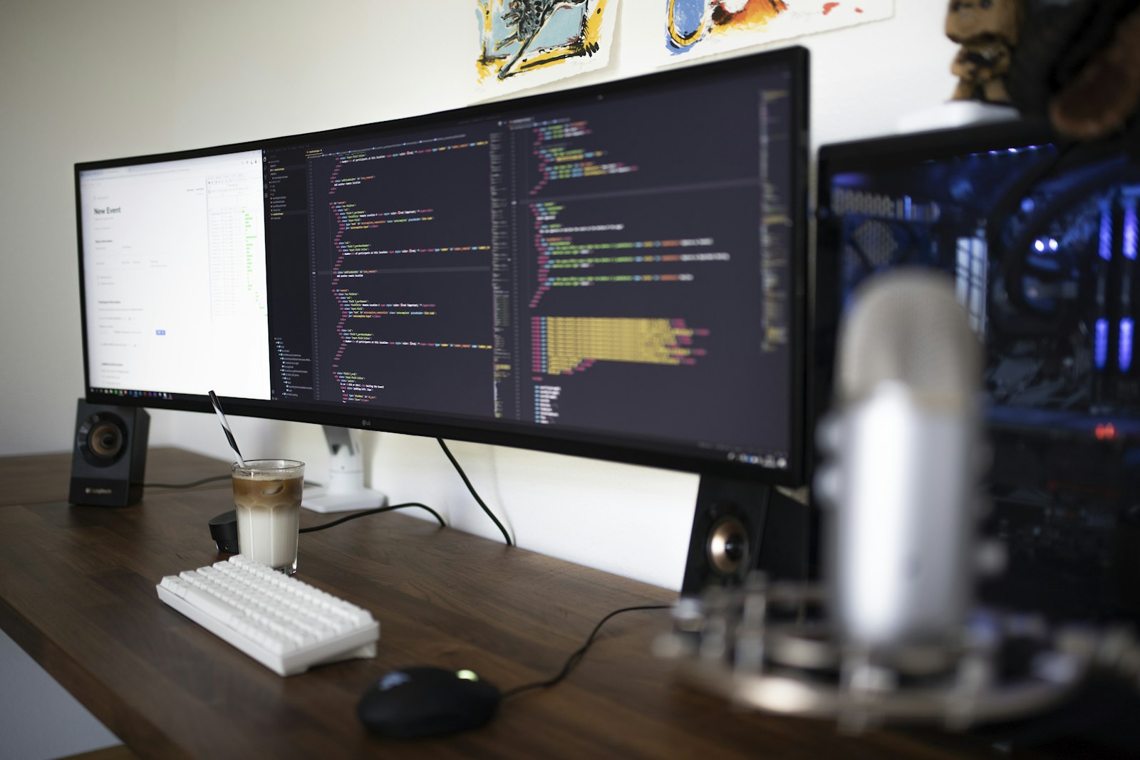 A wide curved monitor showing code beside a keyboard and microphone on a desk
